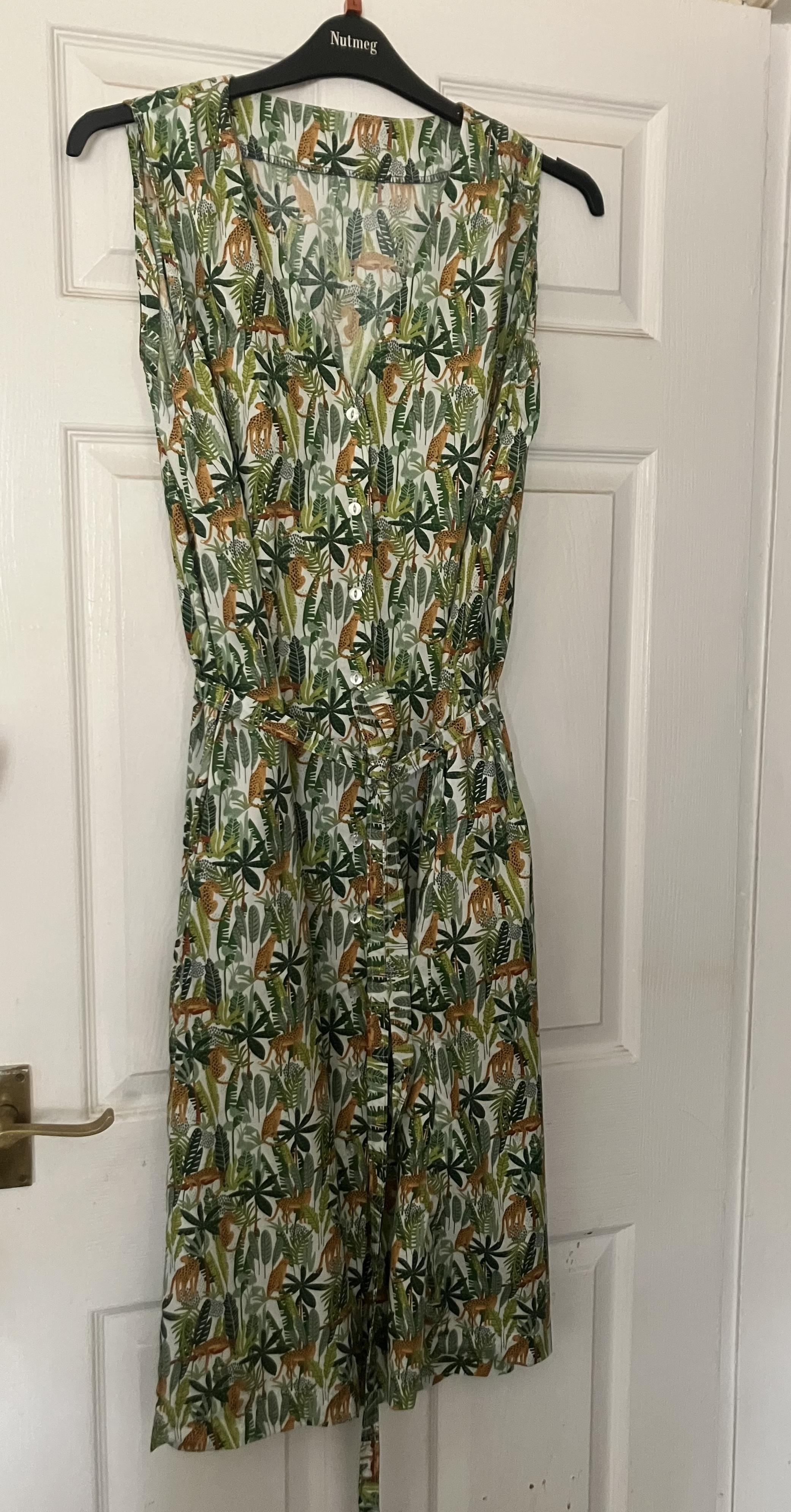 A dress hanging on a door. It is a green jungle print with small orange leopards with black spots all over on a white background